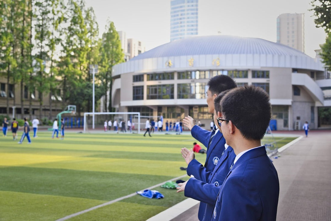 Students watch a soccer game on a school field.
