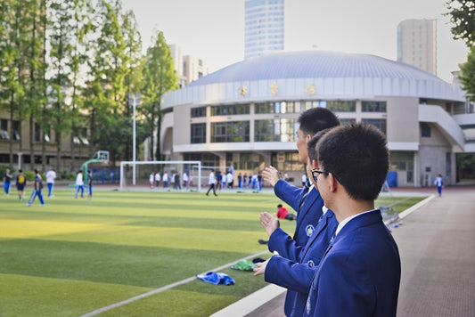 Students watch a soccer game on a school field.