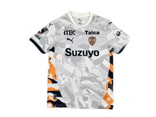 Shimizu S-Pulse 2026/27 away jersey front view, light grey camo pattern, Suzuyo sponsor across chest, club crest, sleeve patches, orange and navy side blocks